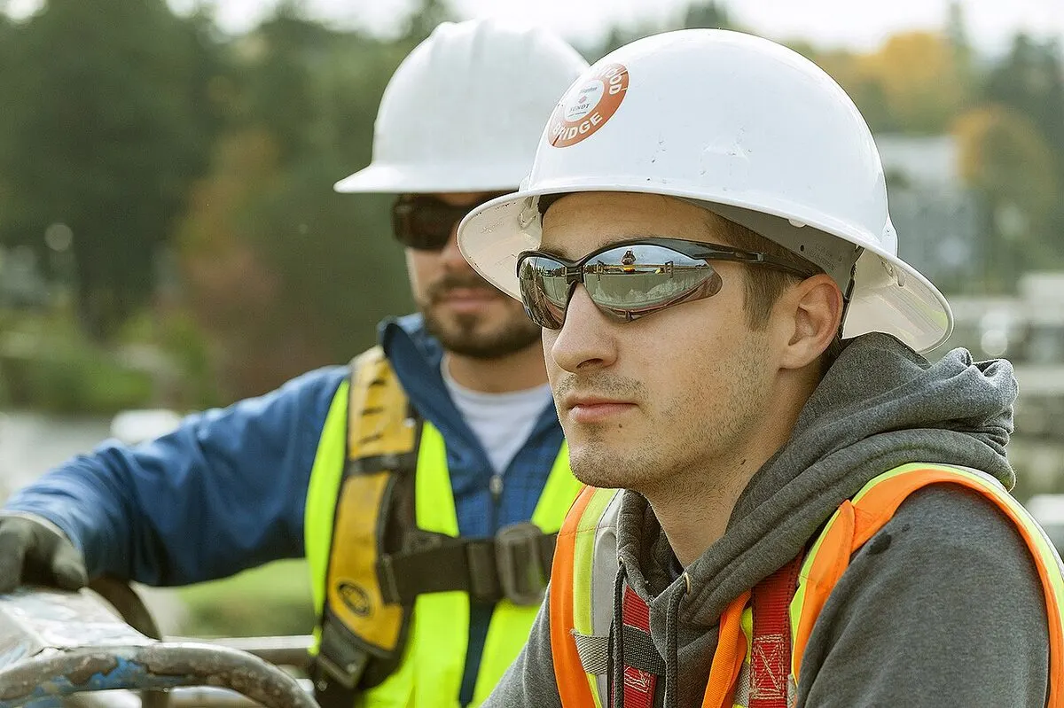 Apprentice electrician in a white hard hat and safety glasses at a worksite