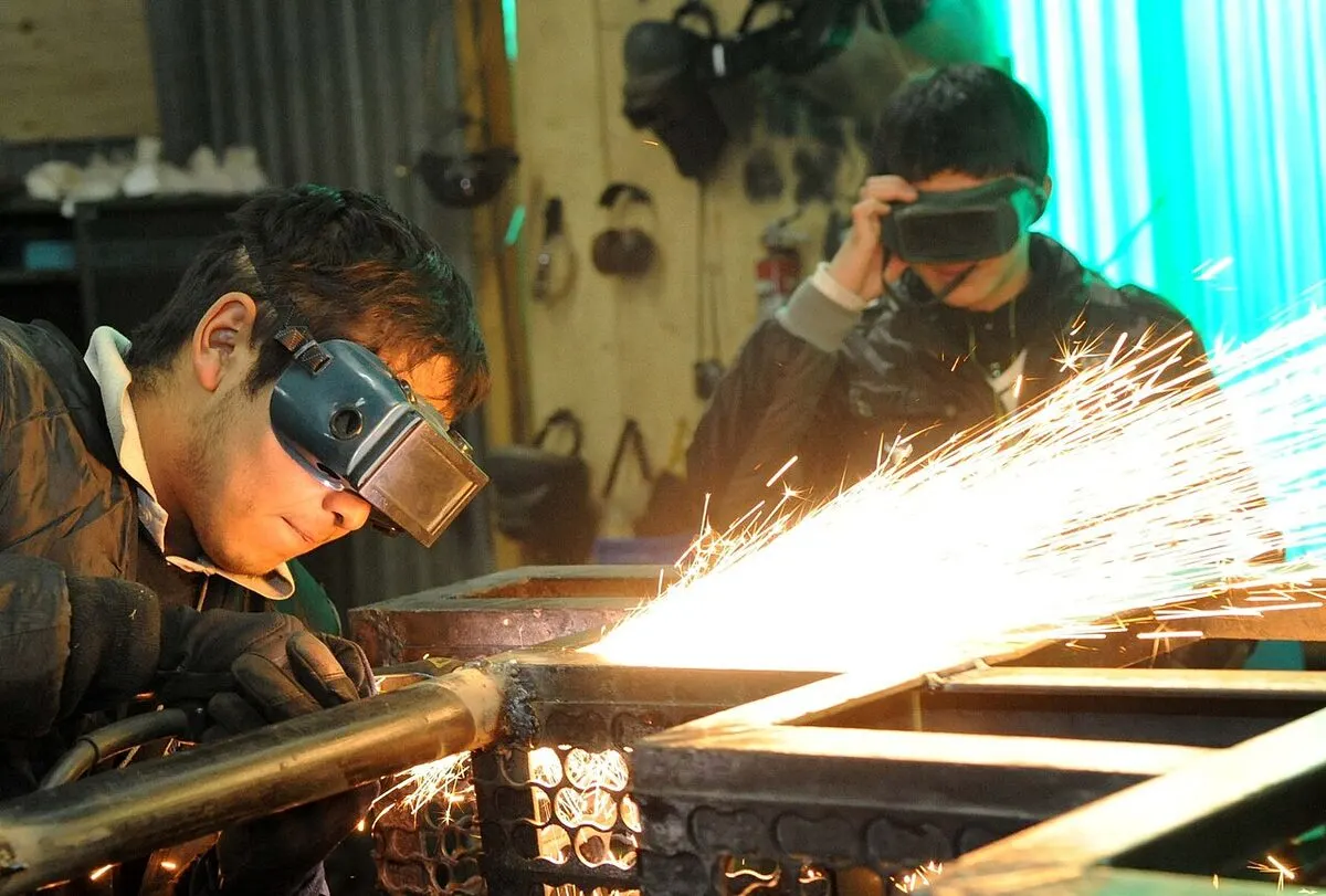 Two vocational students welding metal with protective goggles and sparks flying